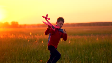 Der-Junge-Im-Kostüm-Eines-Superhelden-Läuft-In-Einem-Roten-Mantel-Und-Lacht-Bei-Sonnenuntergang-Auf-Einer-Sommerwiese-Und-Stellt-Sich-Vor,-Er-Sei-Der-Pilot-Des-Flugzeugs